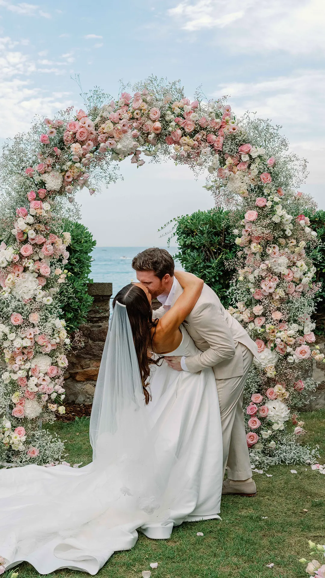Weddings 4 Couple embracing under floral arch.